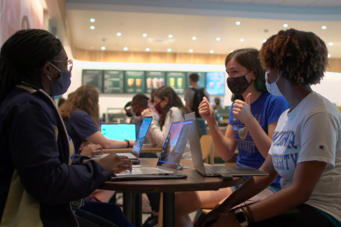 Students sit at tables in Starbucks working on their laptops