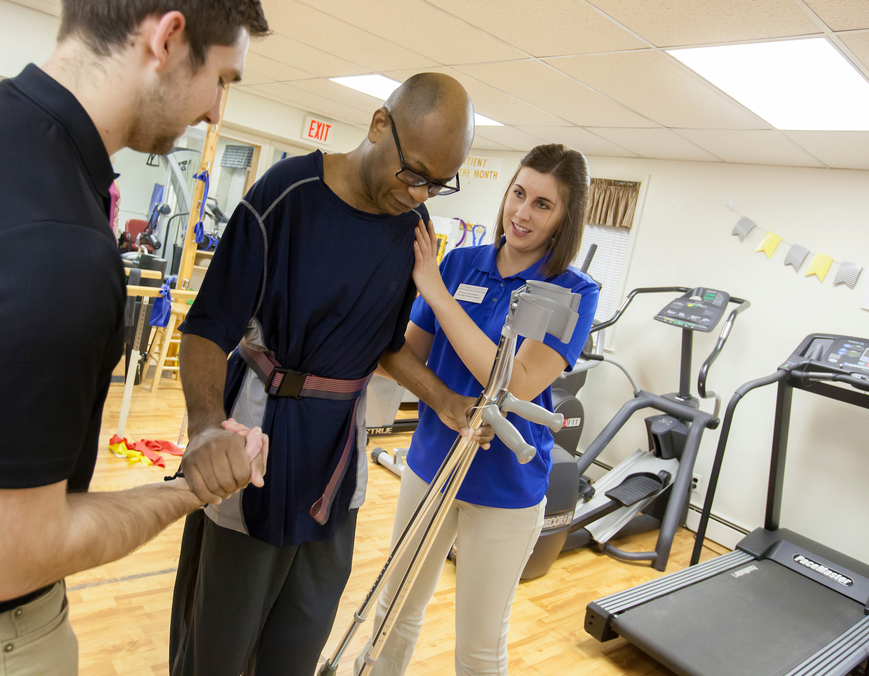 William Beachem standing assisted by two physical therapy students