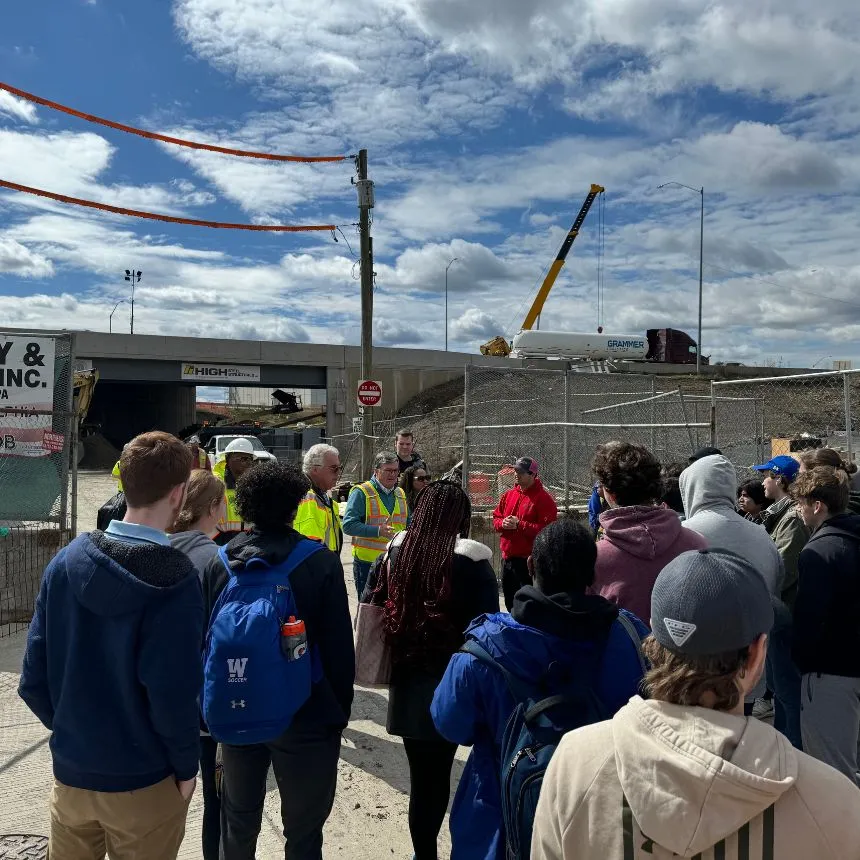 Students stand at the construction site and listen to a project overview from Robert Buckley and Sec. of Transportation Mike Carrol.