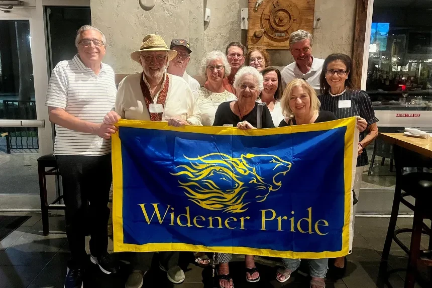 Alumni at a happy hour event pose for a photo with a "Widener Pride" flag