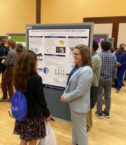 Amanda DiAlessandro stands in front of her research poster and talks with a conference attendee.
