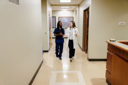 Two health-sciences students walking down a hallway, dressed in scrubs and a white coat