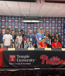 Students pose for a photo in front of a press background with Phillies branding on it