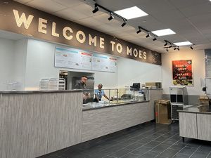 Interior of the Moe's location on campus with a sign that says "Welcome to Moe's" and two people working behind the counter