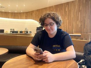 Student sitting at a table in the campus coffee shop looking at their phone