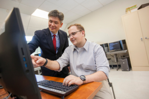 Widener University computer science professor Suk-Chung Yoon stands next to a student on the computer.