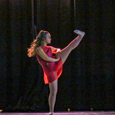 Amanda Rappa on a dark stage in a dance uniform with her leg in the air
