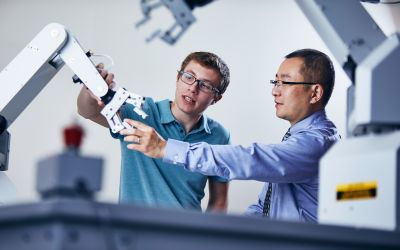 School of Engineering, one of the top engineering schools, bachelor's of robotics student and professor with robotic arm. Robotics is one of the many engineering fields Widener offers engineering programs.