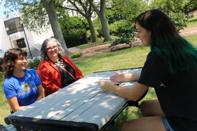 Two students and a faculty member sit outside at a picnic table