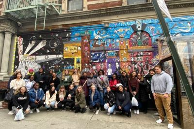 Large group of Widener students standing in front of a colorful mural in Harlem.