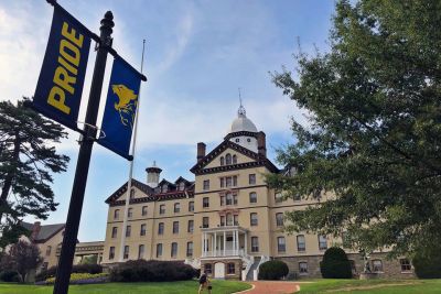 A photo of Old Main with a blue and gold banner in the foreground that reads "Pride"