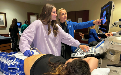 A student and an instructor use an ultrasound machine in training on another student who is playing the role of patient. 