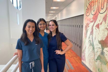 Three female PA students in scrubs stand together for a photo.