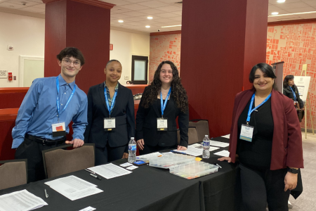 Students and a faculty member pose for a photo at the conference check in table. Everyone is smiling at the camera.