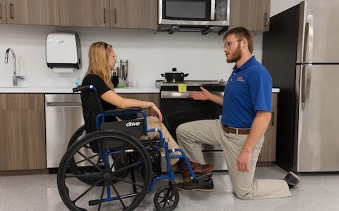 Occupational therapy student works with a wheelchair user in a Daily Activities Lab, practicing independent living skills and activities of daily living.