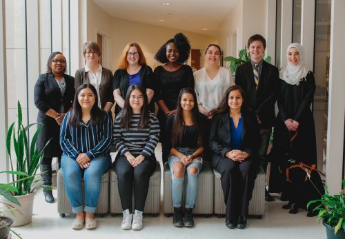 11 students and faculty members in professional clothes sit in two lines