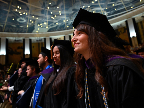 Graduates in the crowd stare off screen, smiling.