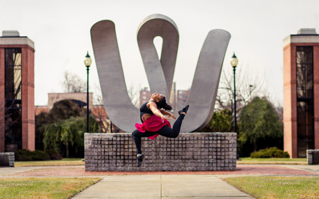 Dance student in a mid-air jump in front of the 'W' statue