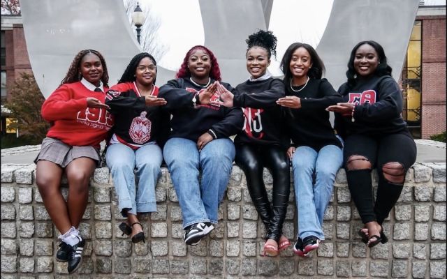 Members of Delta Sigma Theta Sorority, Inc. sitting on a W statue on Widener University’s campus during a group photo.