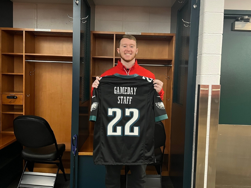 Tiernan poses holding a Philadelphia Eagles jersey that reads "gameday staff"